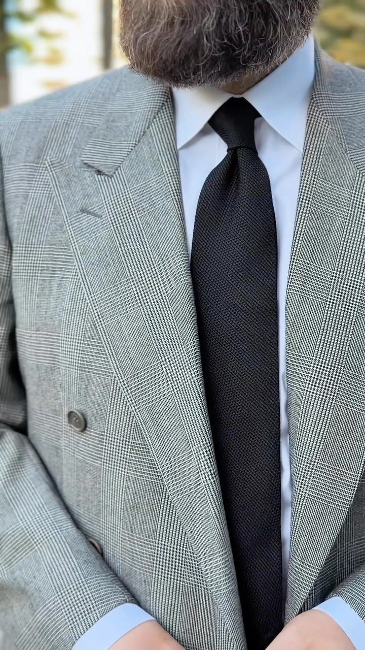 A man wearing a grey patterned suit, white shirt, and black textured tie.
