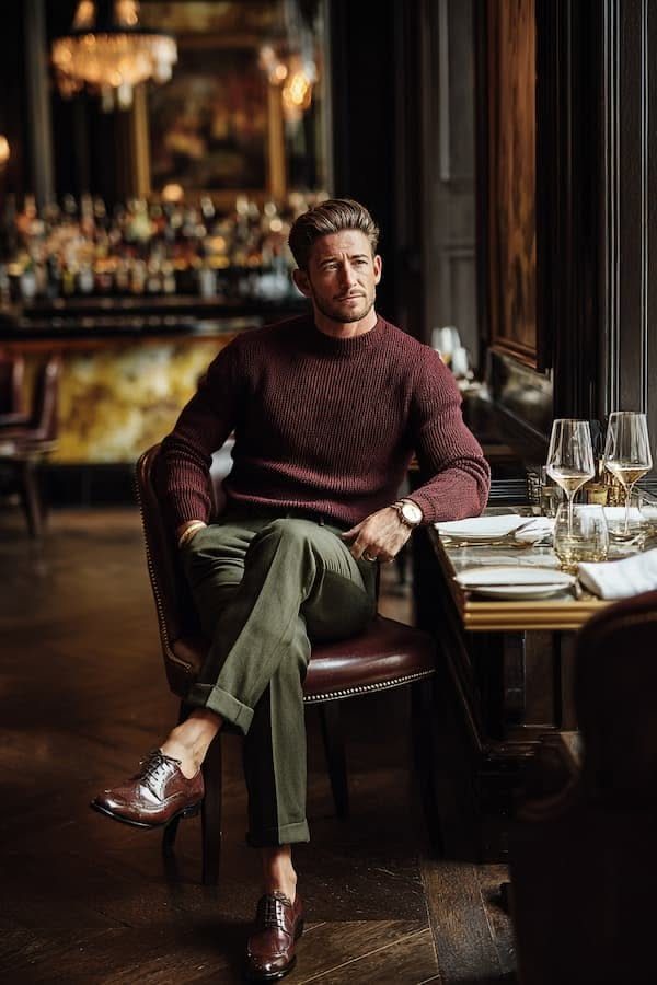 A man in a burgundy sweater and olive green trousers sitting in a restaurant.