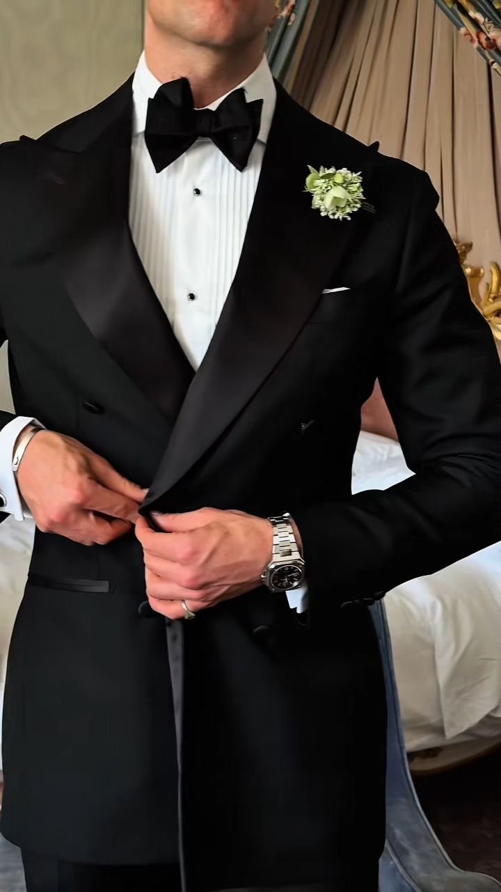 Man in a black double-breasted tuxedo adjusting his jacket with a white boutonniere.