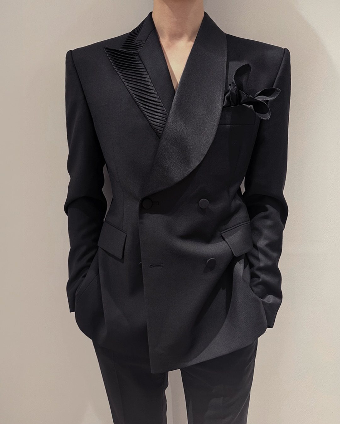 A man wearing a black double-breasted blazer with pleated satin lapels and a pocket square.