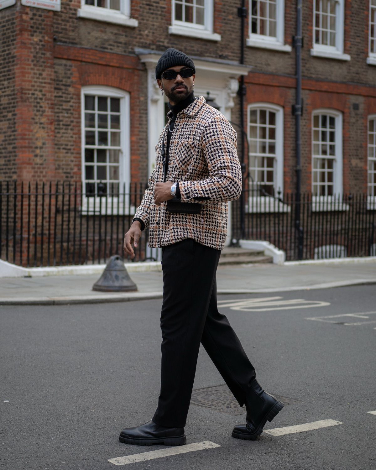 Man walking down a city street wearing a patterned shirt, black trousers, and black boots.