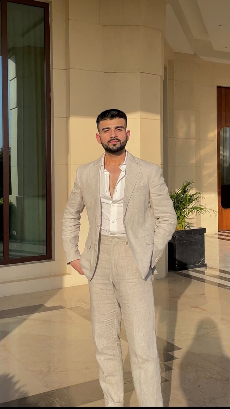A man posing in a light beige linen suit and white shirt outdoors.