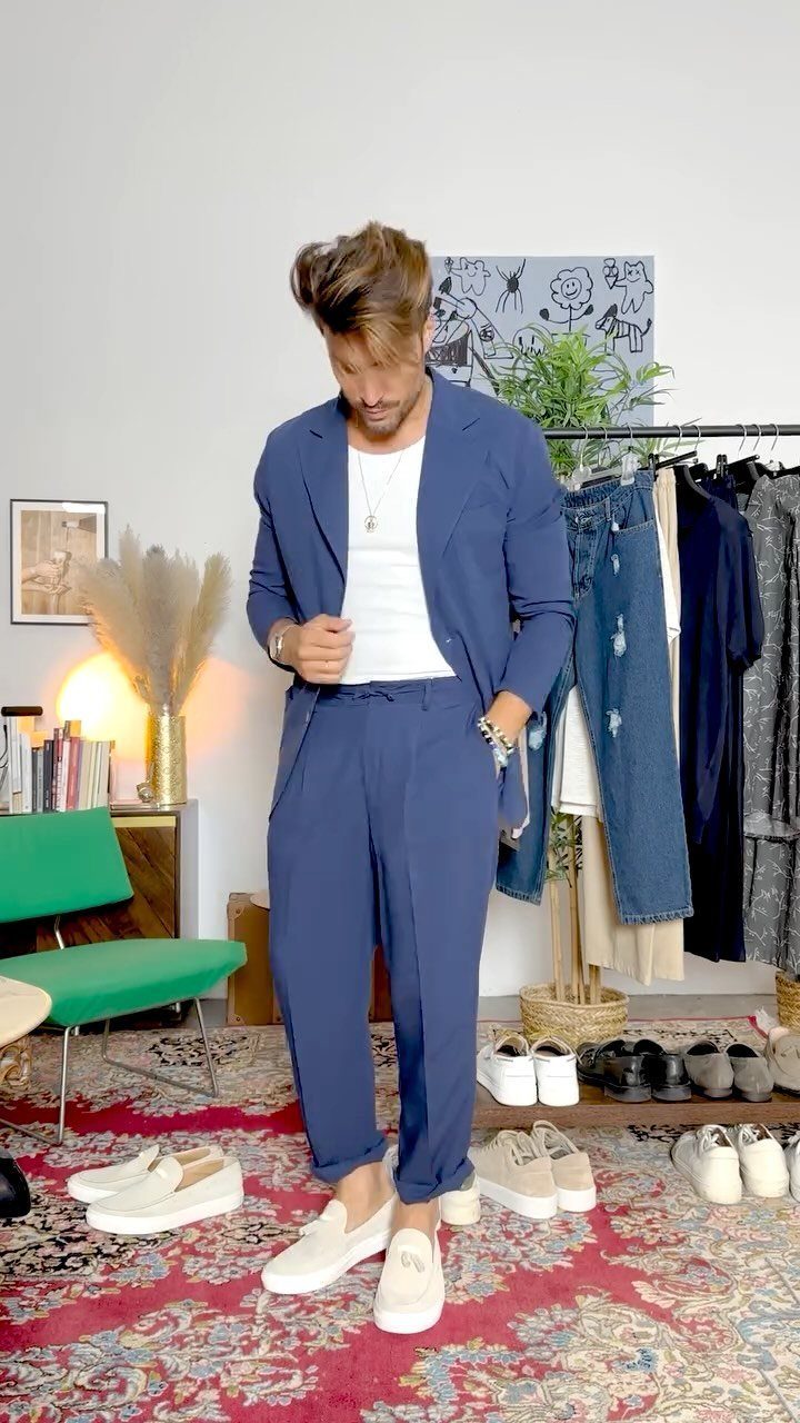 A man posing in a navy blue linen suit with white t-shirt and loafers.