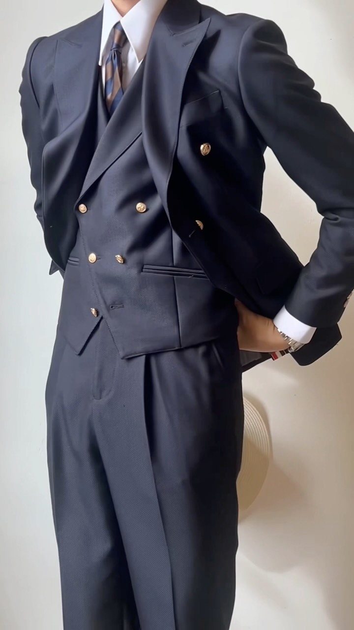A man posing in a navy blue double-breasted suit with gold buttons and a patterned tie.