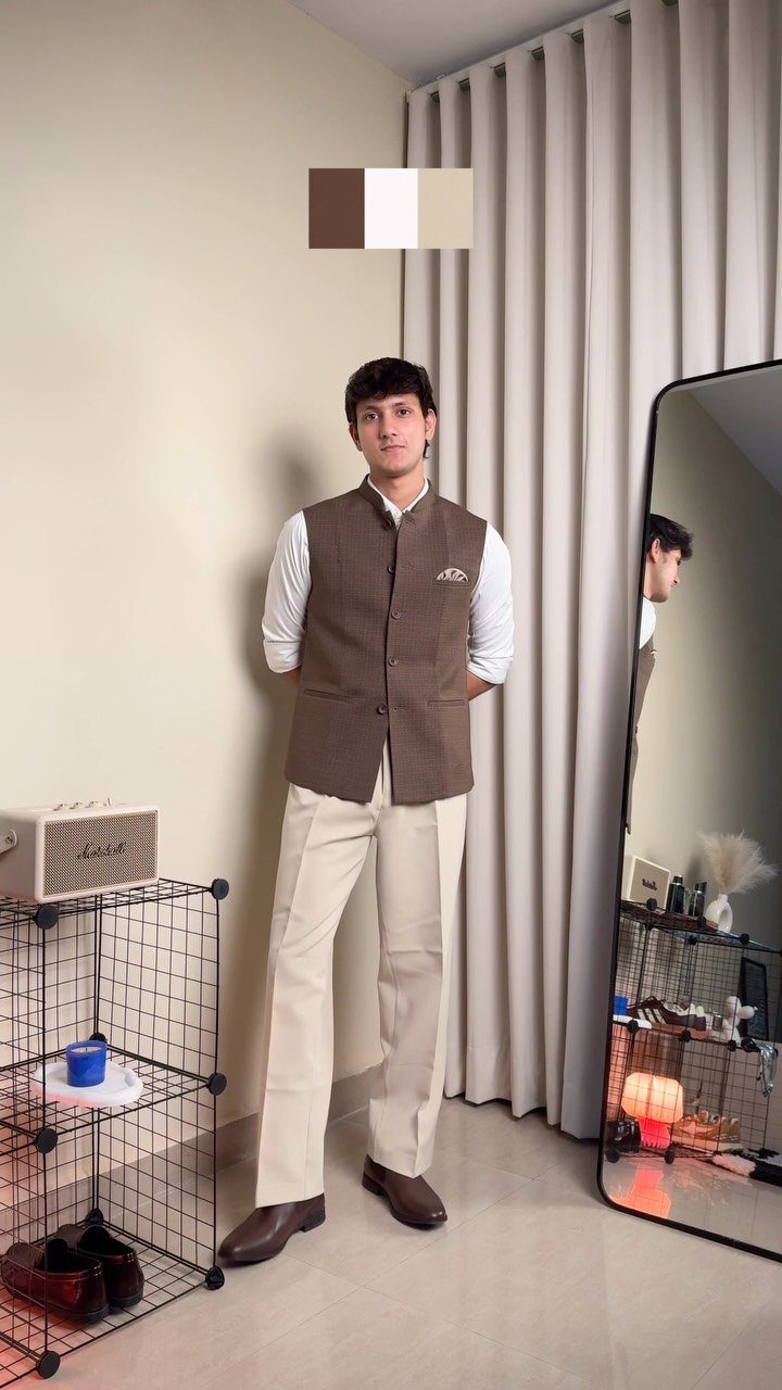 A man posing in a brown waistcoat, white shirt, and cream trousers.