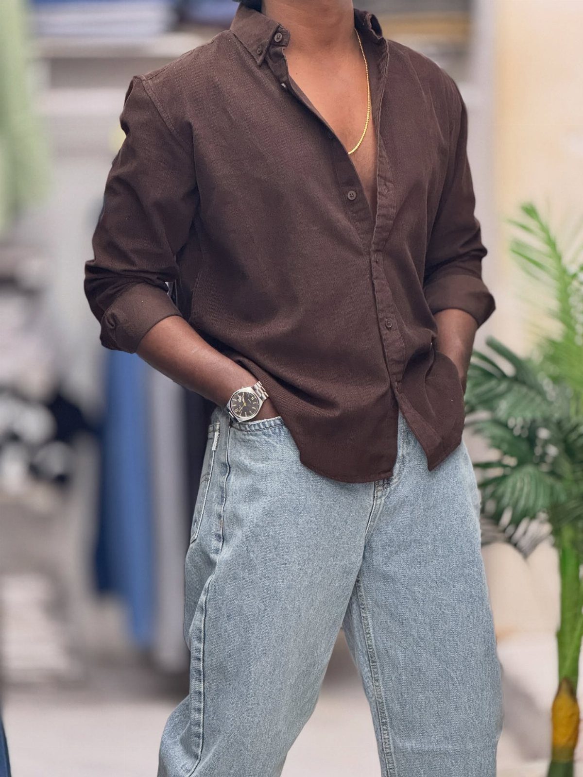 Man wearing a brown button-down shirt and light blue denim jeans with a silver watch.