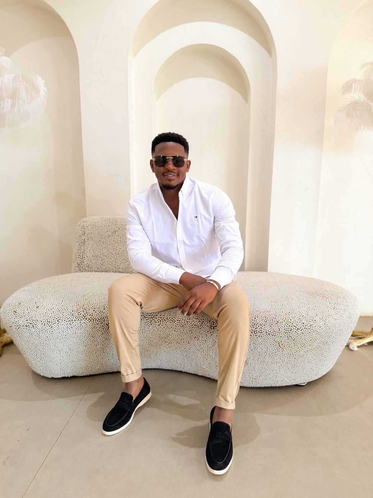 A man sitting on a white bench wearing a white shirt and tan chinos.