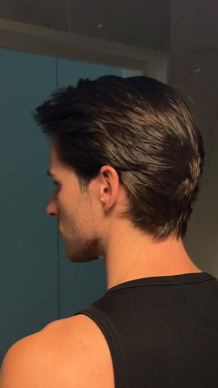 A man with styled dark hair and light facial stubble shown in profile.