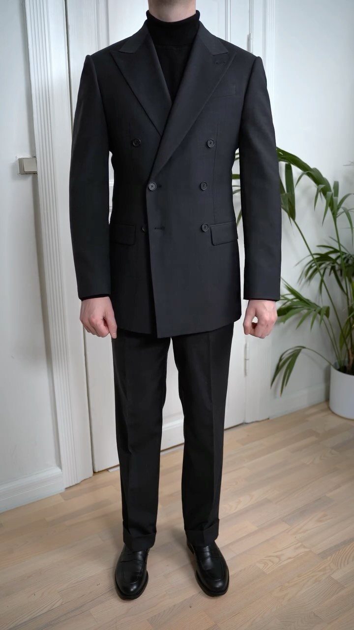 Man wearing a charcoal double-breasted suit with a black turtleneck and black dress shoes.