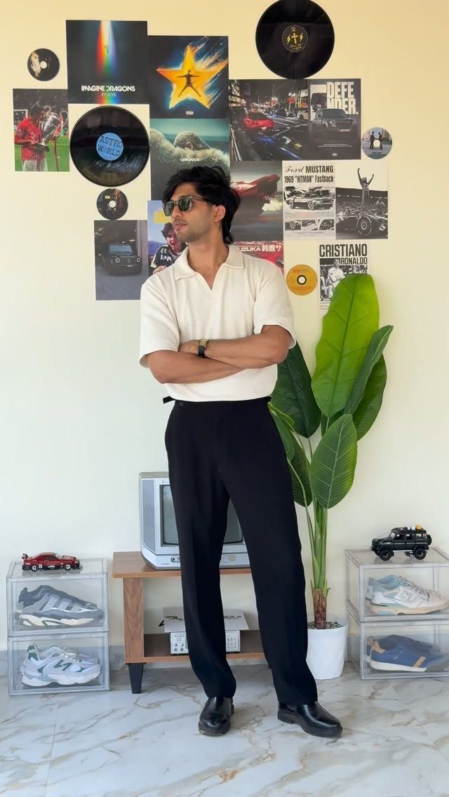 Man in a cream polo shirt and black trousers standing against a wall of vinyl records.