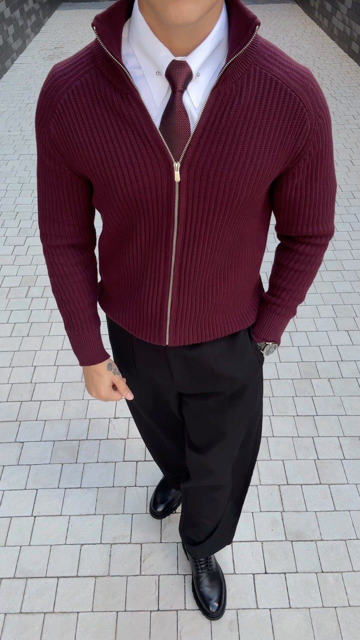 Man wearing a burgundy ribbed cardigan over a white shirt and tie with black trousers.
