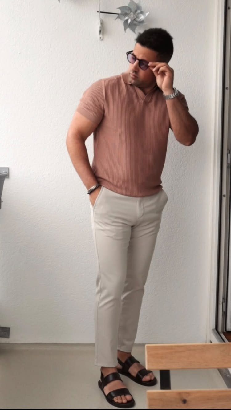 Man in a mauve polo shirt and beige trousers posing against a white wall.