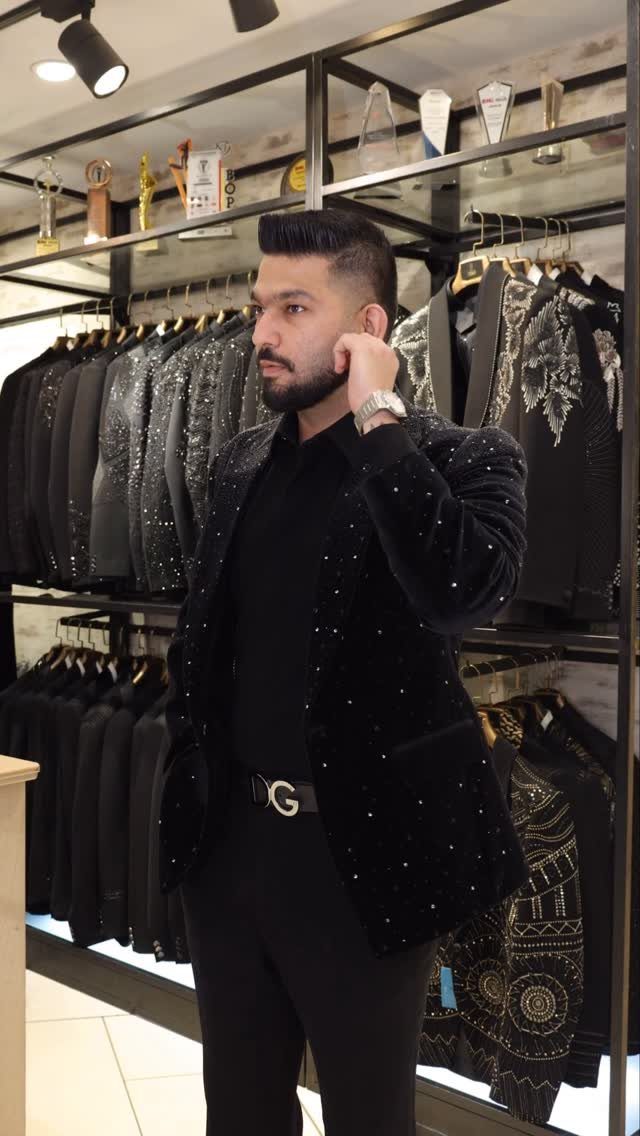 A man posing in a black velvet embellished blazer and black clothing inside a boutique.