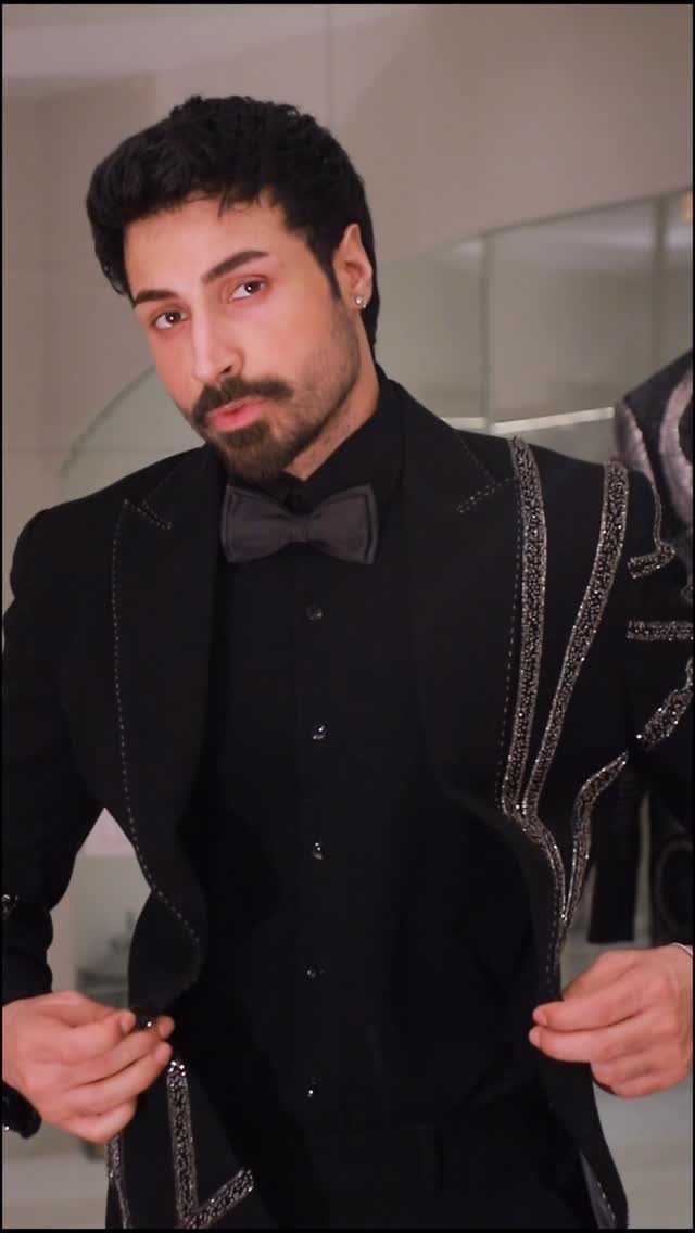 A man posing in a black sequined tuxedo jacket with a matching bow tie.