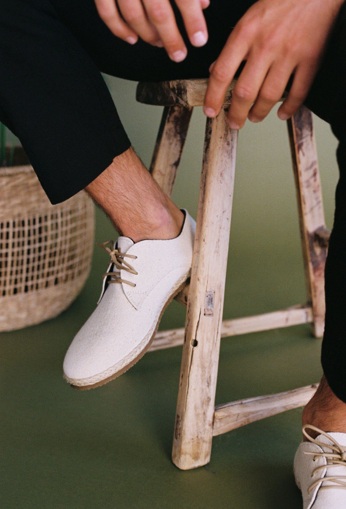 White canvas lace-up derby shoes worn by a person sitting on a wooden stool.