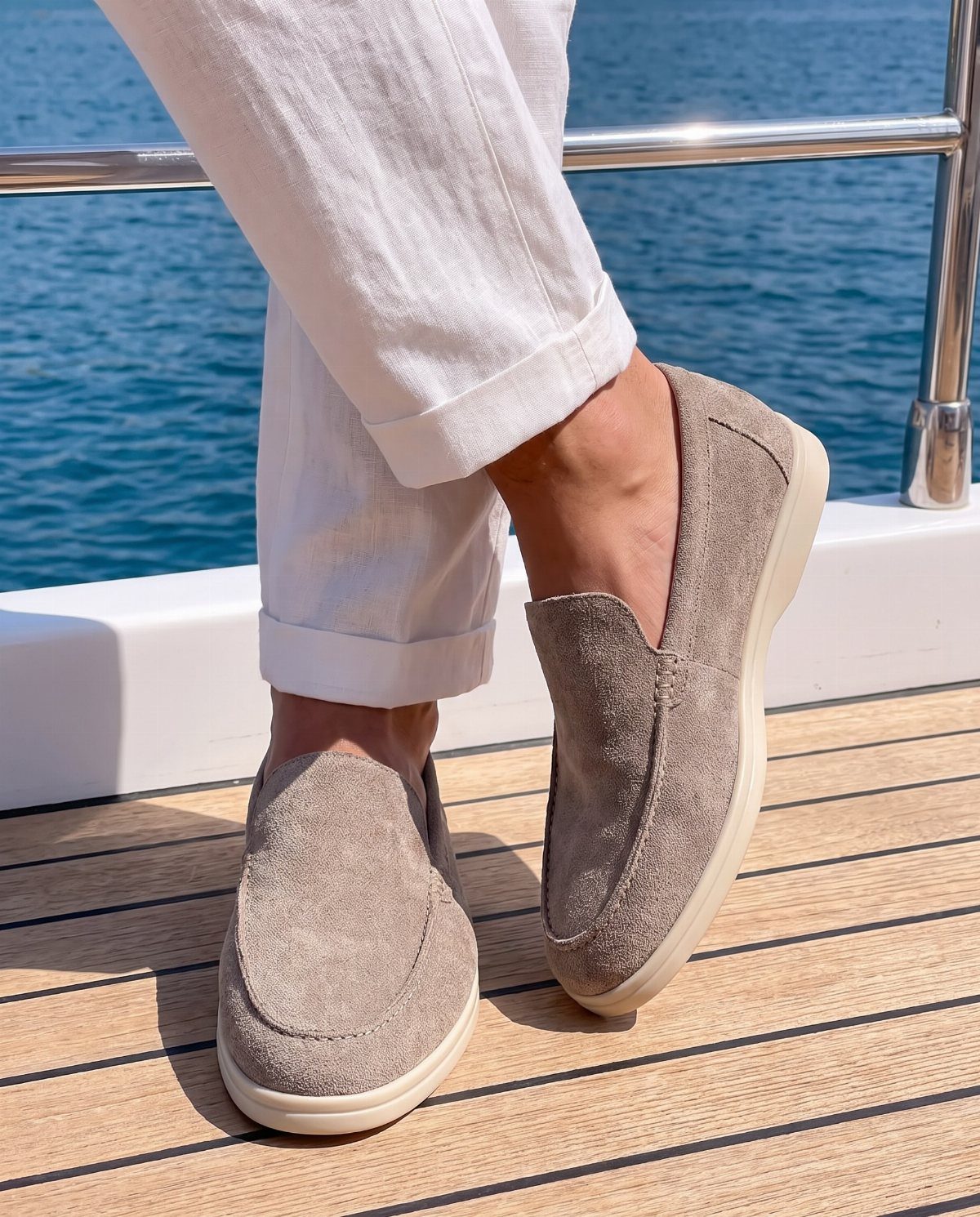 Person wearing beige slip-on loafers and white linen trousers on a wooden boat deck.