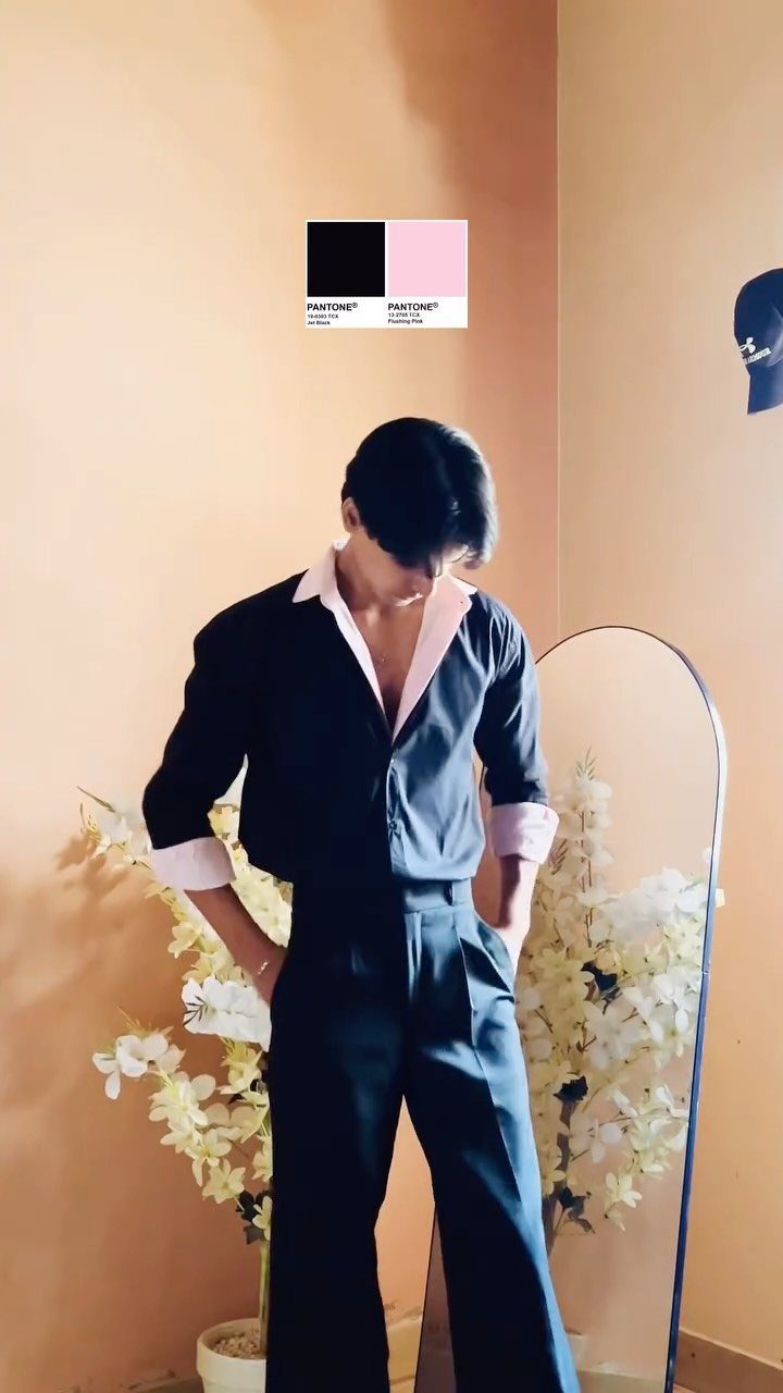 Man wearing a black dress shirt with pink collar and cuffs paired with black trousers.