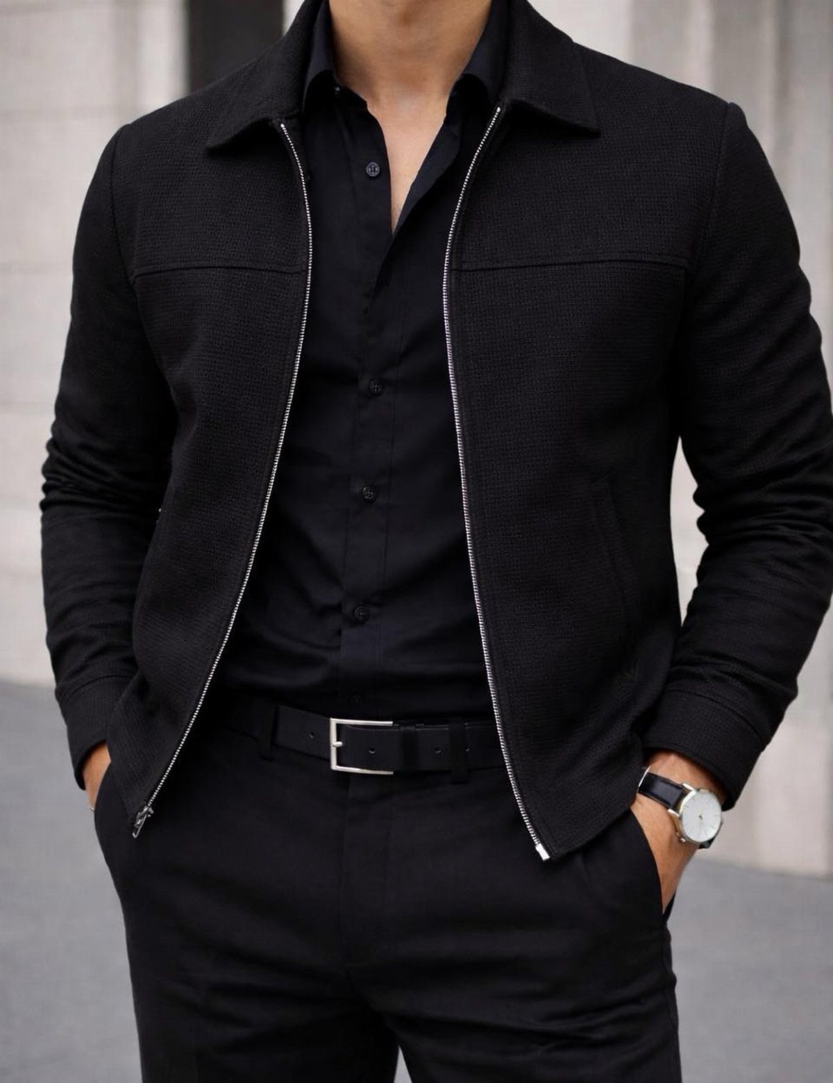 Man wearing a black dress shirt, black trousers, and a textured black jacket with a silver watch.