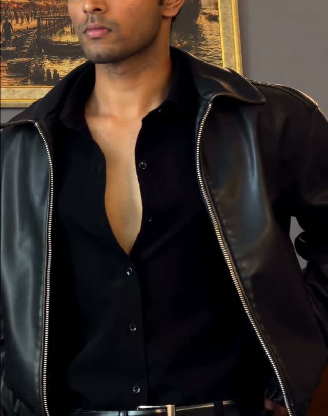 Man wearing an unbuttoned black dress shirt and a black leather jacket.