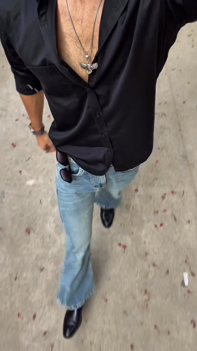 Man walking in a black dress shirt, light blue flared jeans, and black boots.