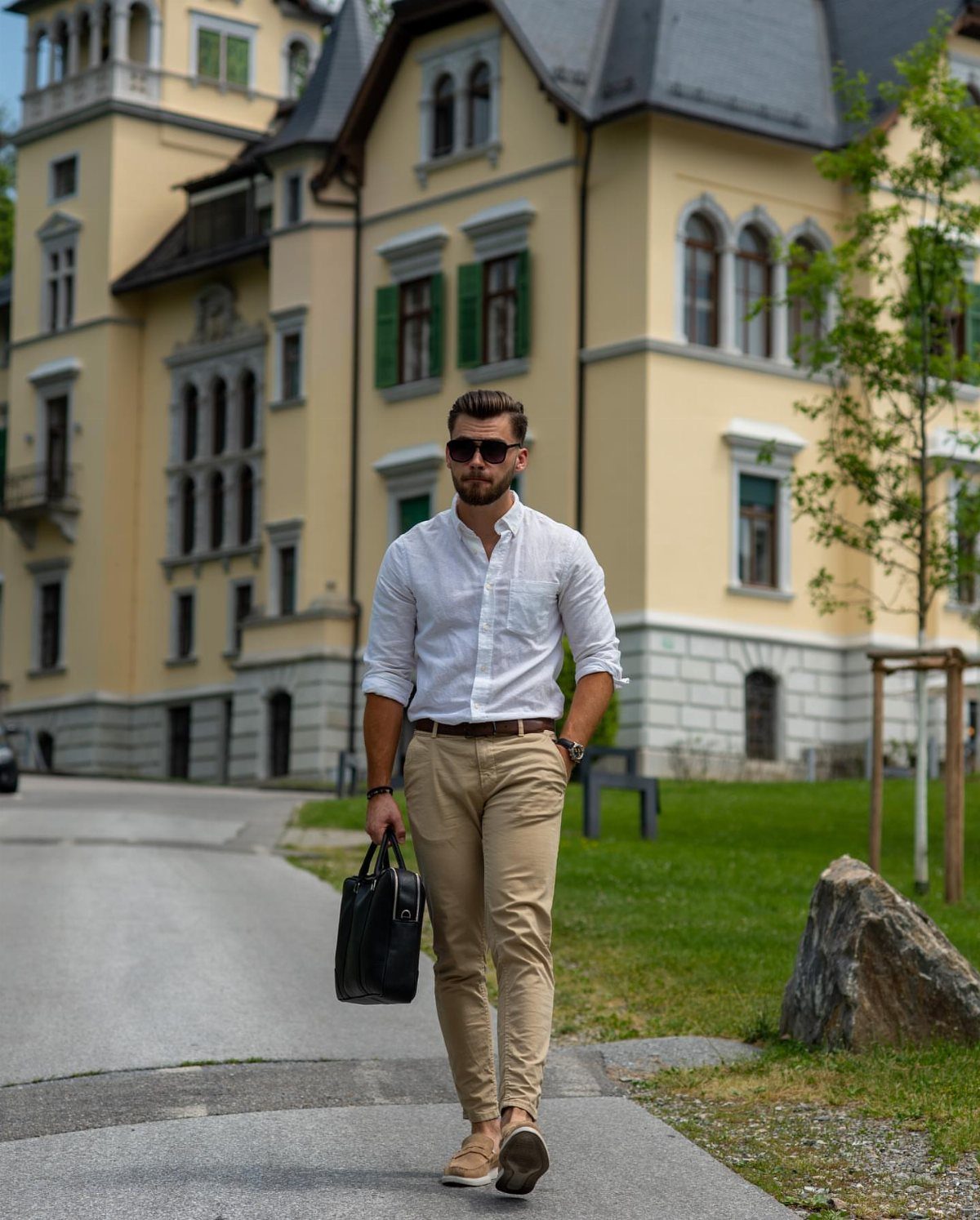Man in white button-up shirt and khaki chinos walking with a black briefcase outdoors.