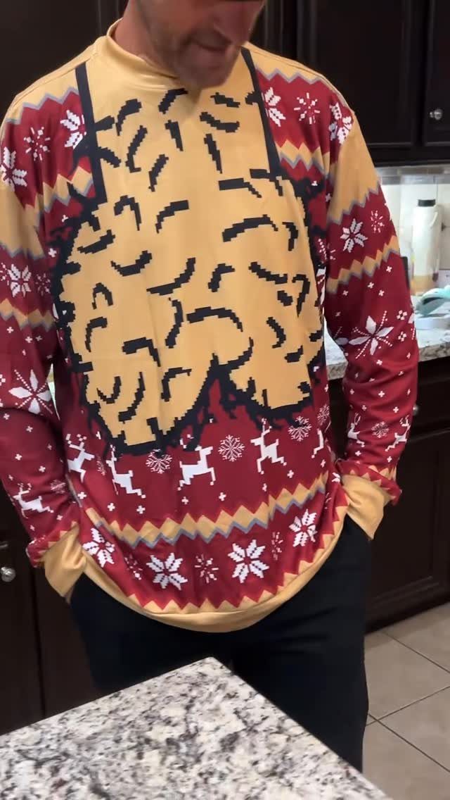 A man wearing a festive red and gold patterned ugly Christmas sweater with a large yellow graphic.