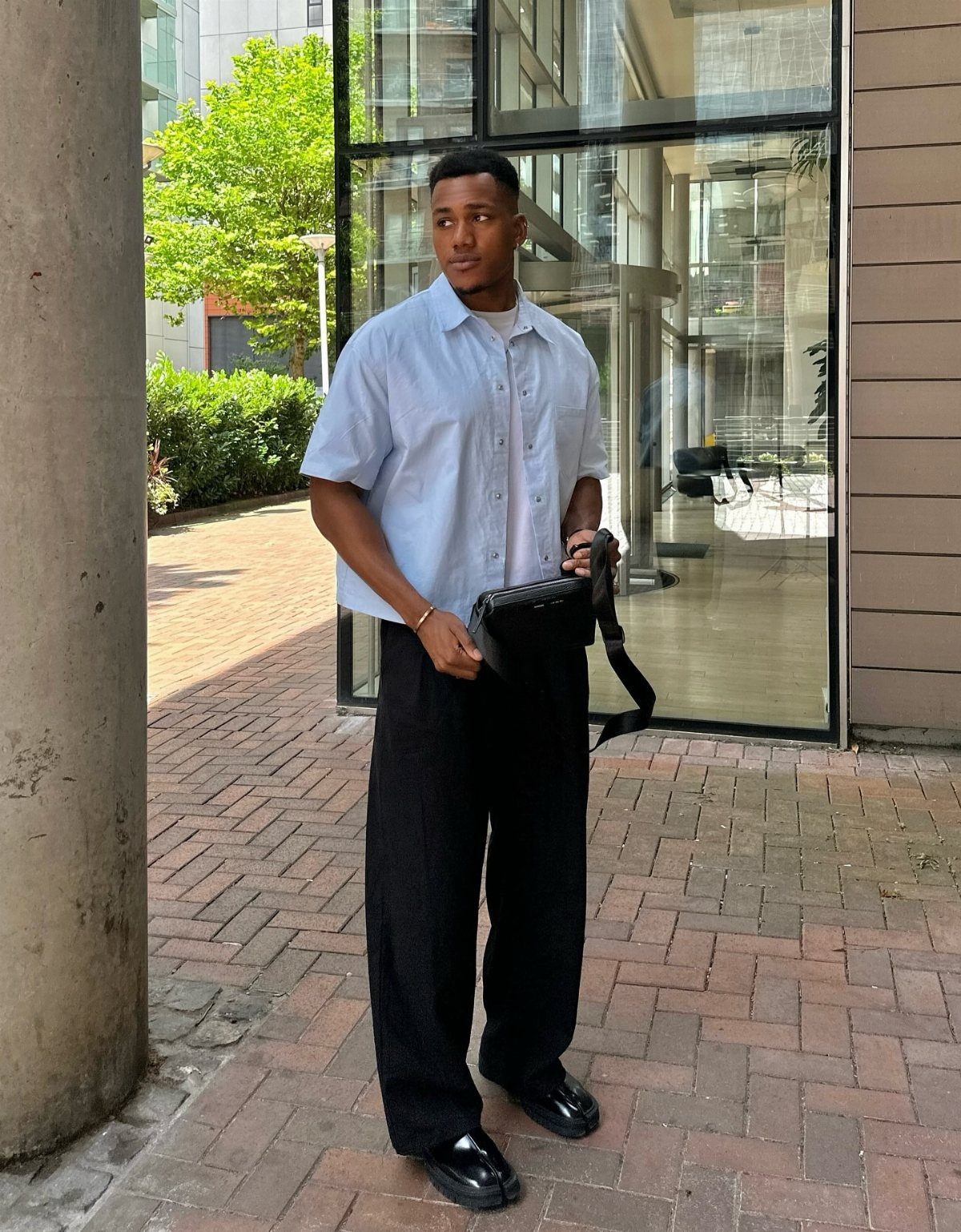 Man wearing a light blue short-sleeve button-down shirt and black wide-leg trousers.