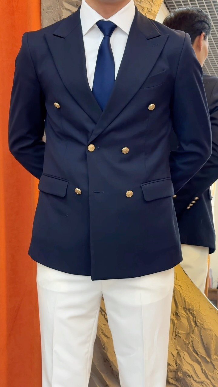 Man wearing a navy double-breasted blazer, white shirt, blue tie, and white trousers.