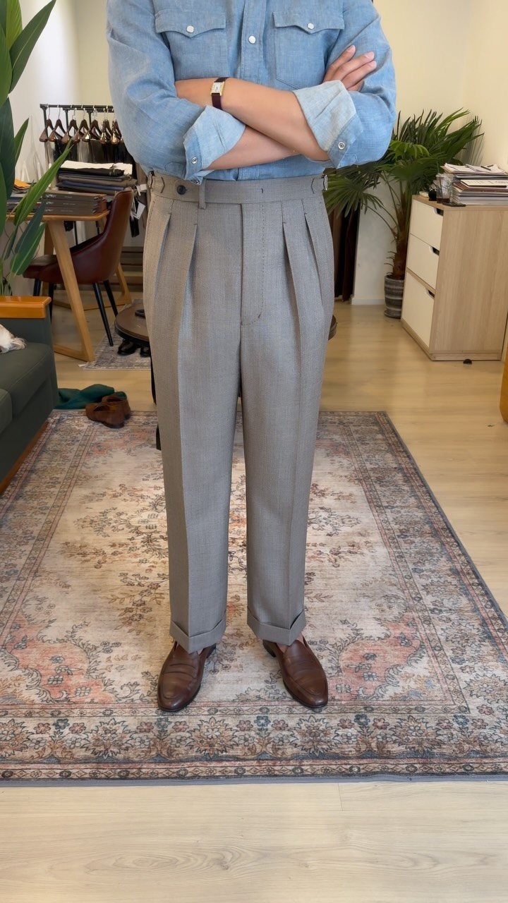 Man wearing a light blue shirt and pleated grey dress trousers with brown leather shoes.