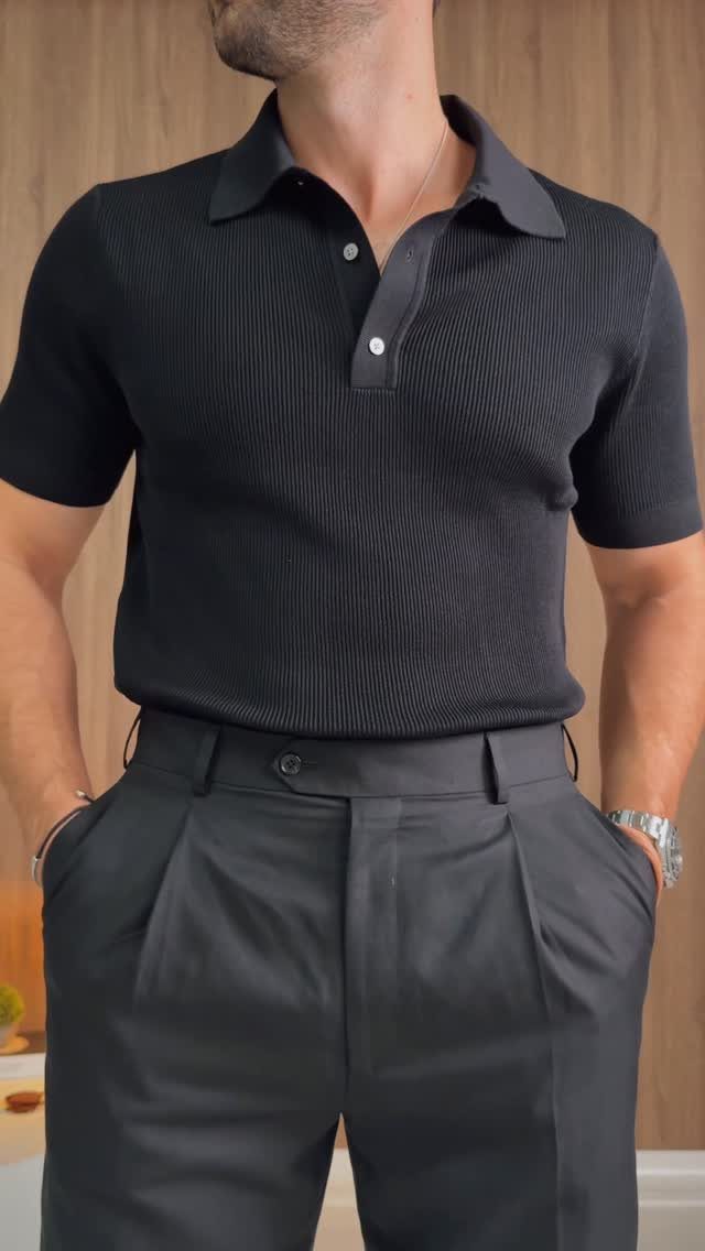 Man wearing a black textured polo shirt and dark grey pleated trousers.