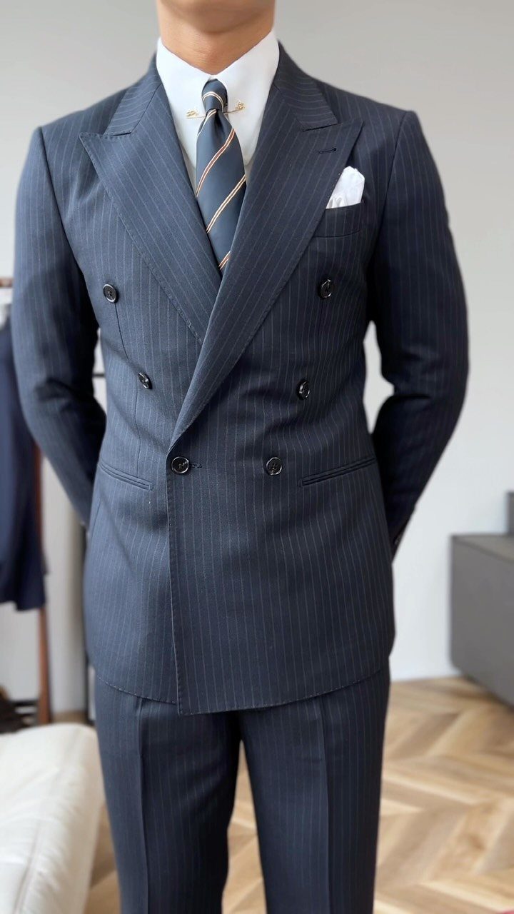 A man wearing a navy blue pinstriped double-breasted suit with a white pocket square.