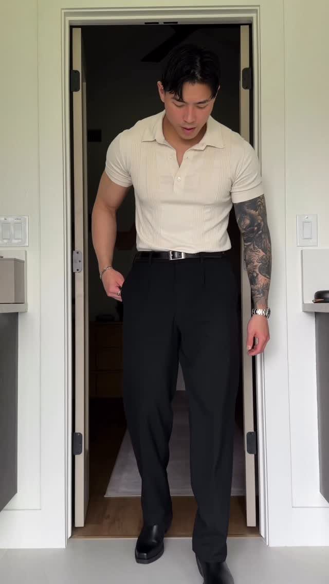 A man wearing a cream polo shirt and black trousers standing in a doorway.