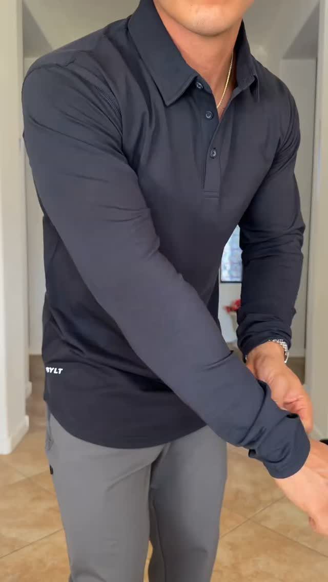 A man wearing a dark navy long-sleeved polo shirt and grey trousers.