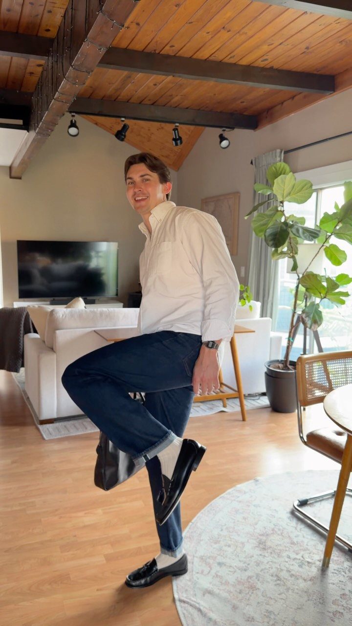A man in a white shirt and dark trousers posing in a bright living room.