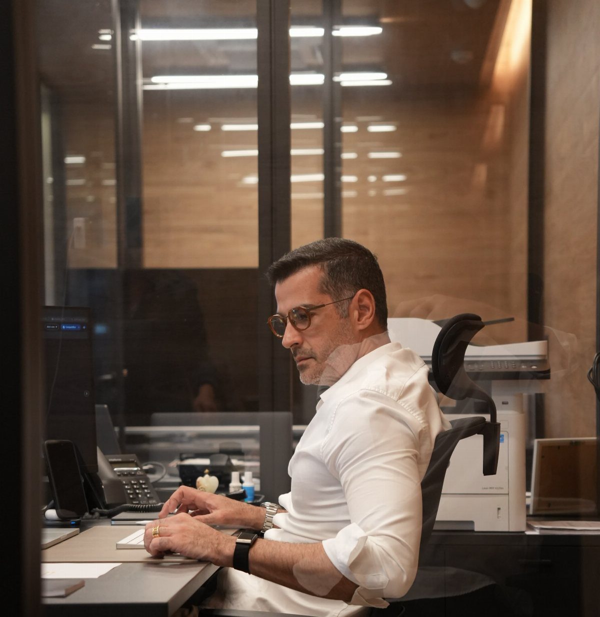 A man in a white button-down shirt working at a desk in a modern office setting.
