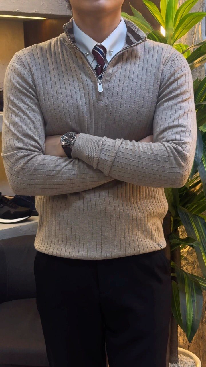 Man wearing a tan ribbed quarter-zip sweater layered over a white shirt and striped tie.