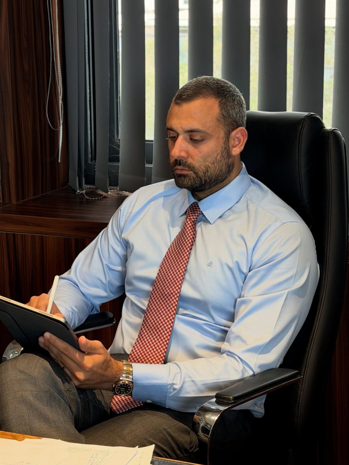 A man in a light blue shirt and red tie writing in a notebook.