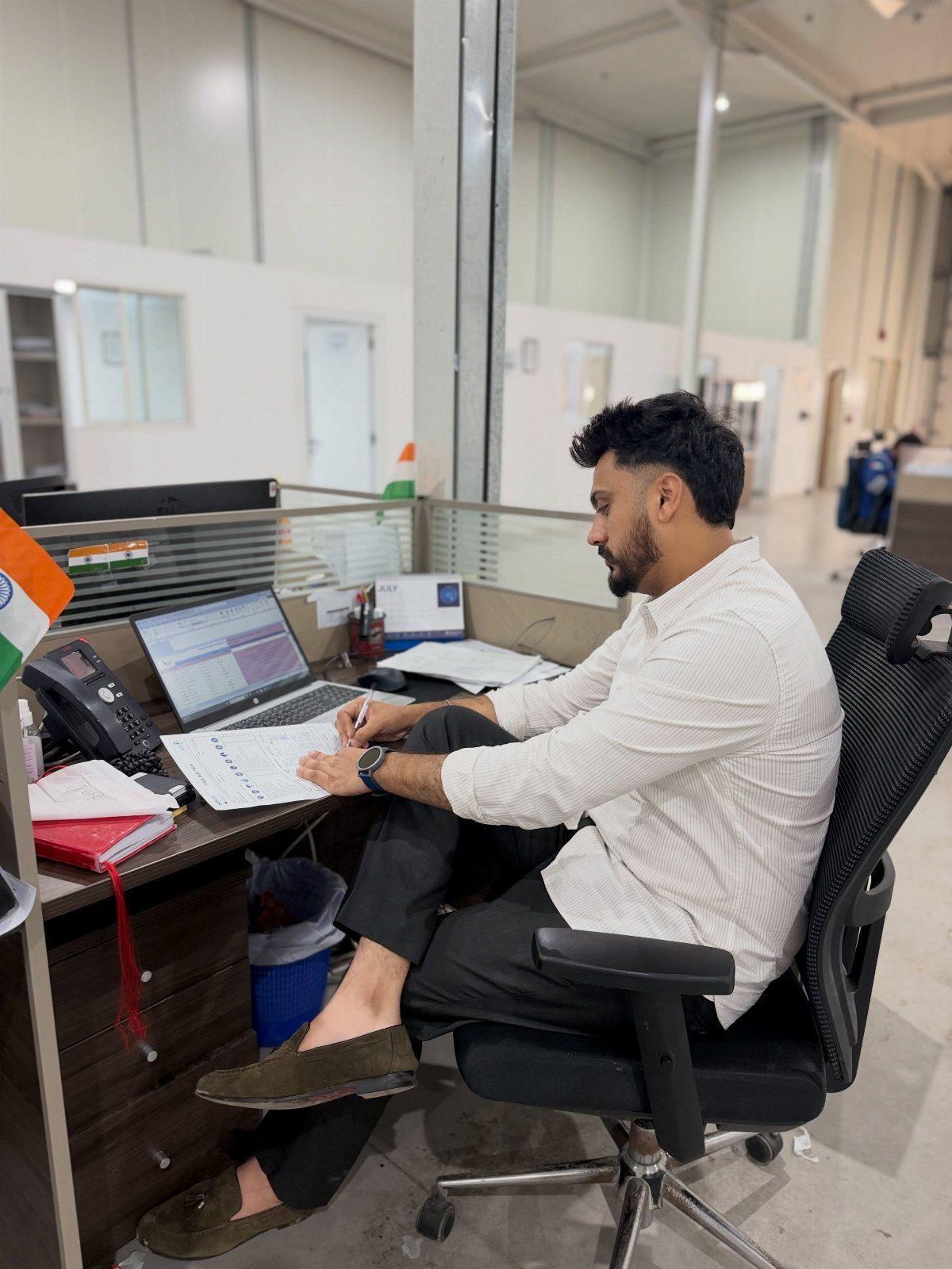 A man in a white shirt and dark trousers working at an office desk.