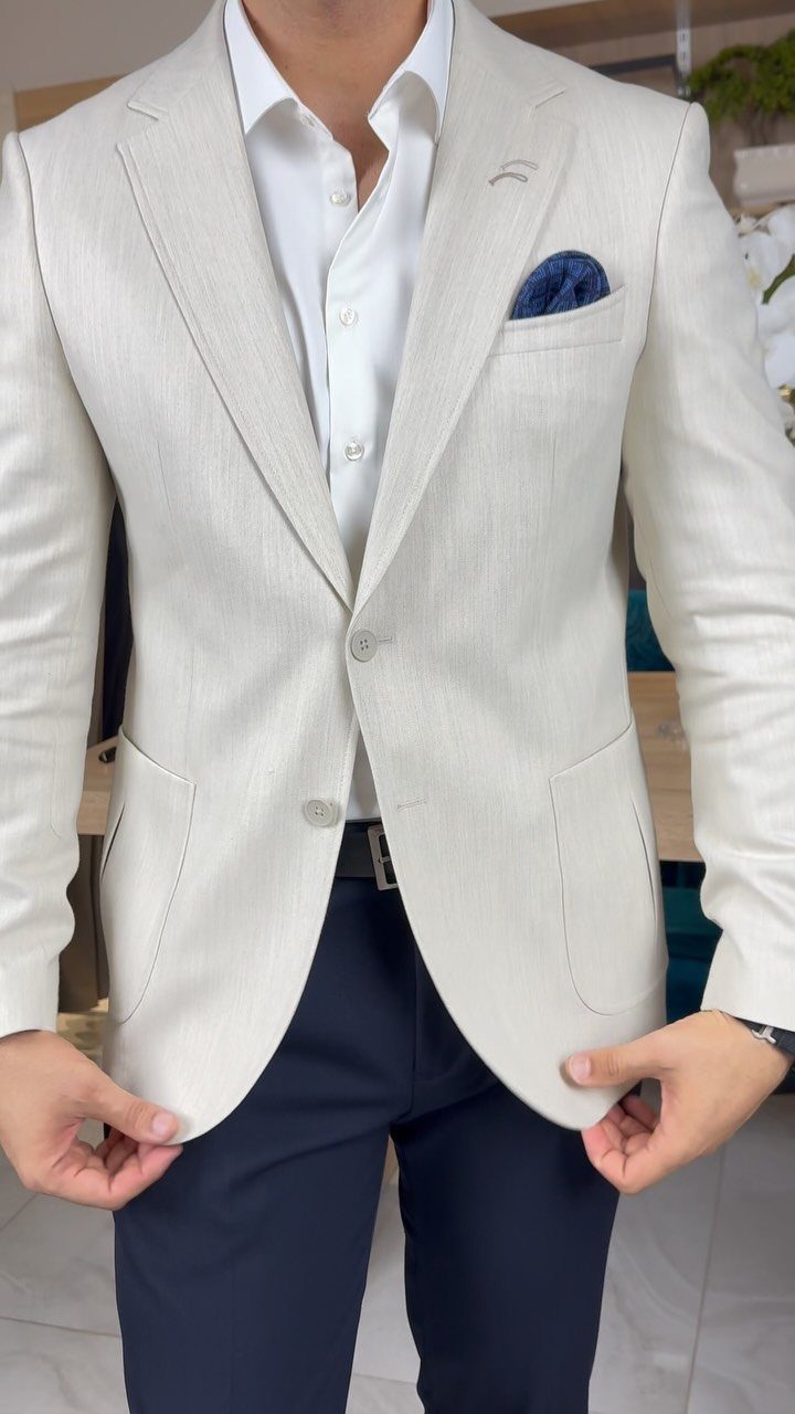 Man wearing a cream linen blazer, white shirt, and navy trousers for a semi casual look.