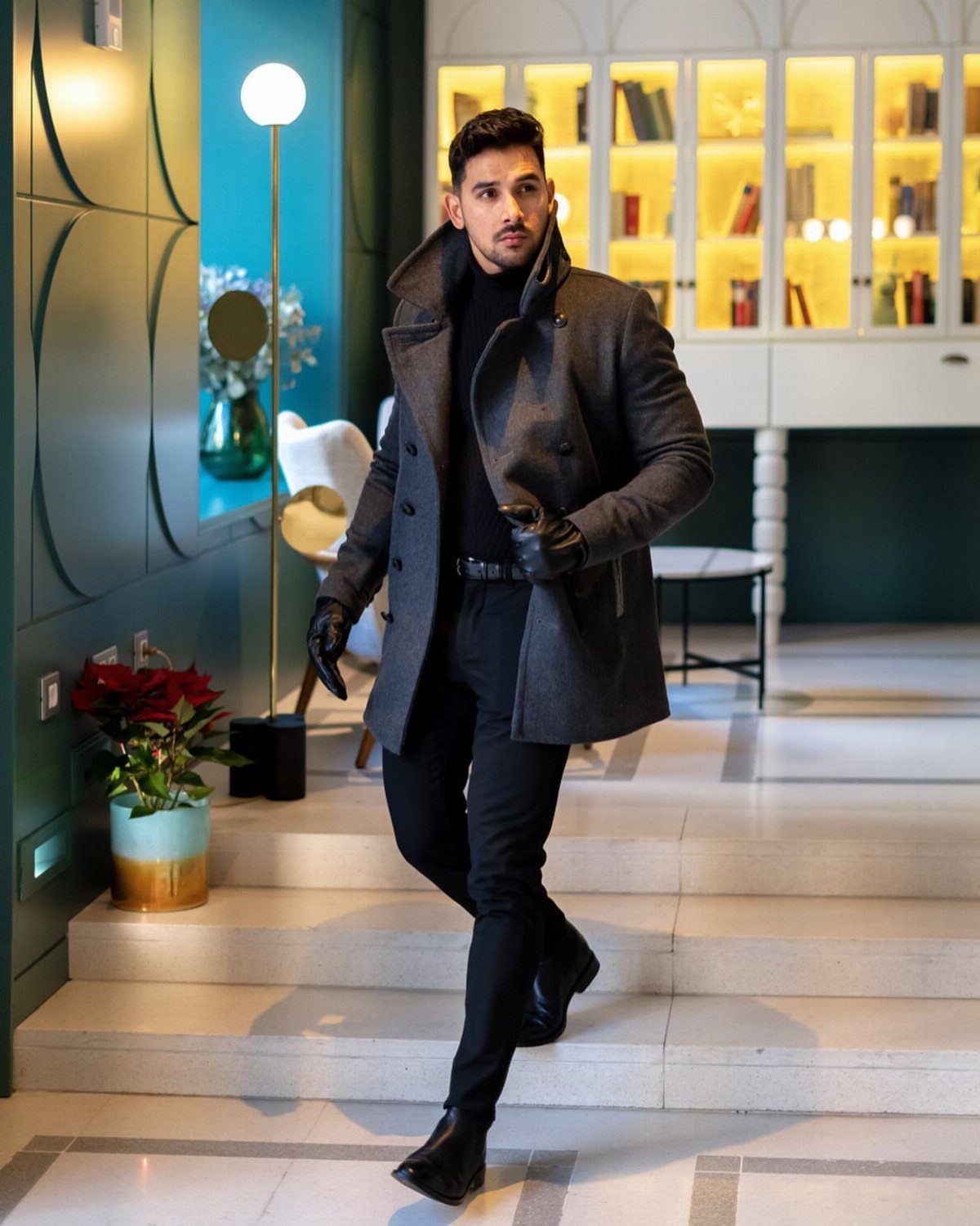 Man in a dark grey overcoat and black turtleneck walking down indoor stairs.