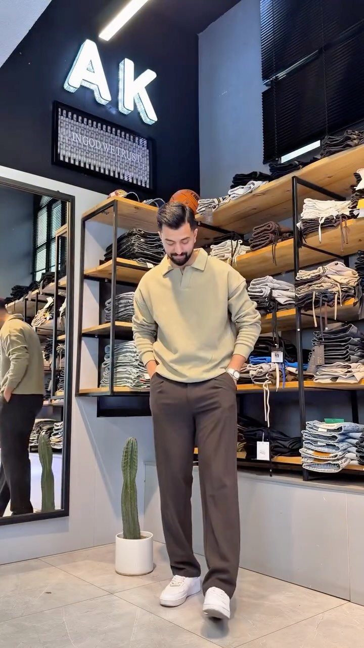 Man wearing a light olive polo shirt, grey trousers, and white sneakers standing in a clothing store.