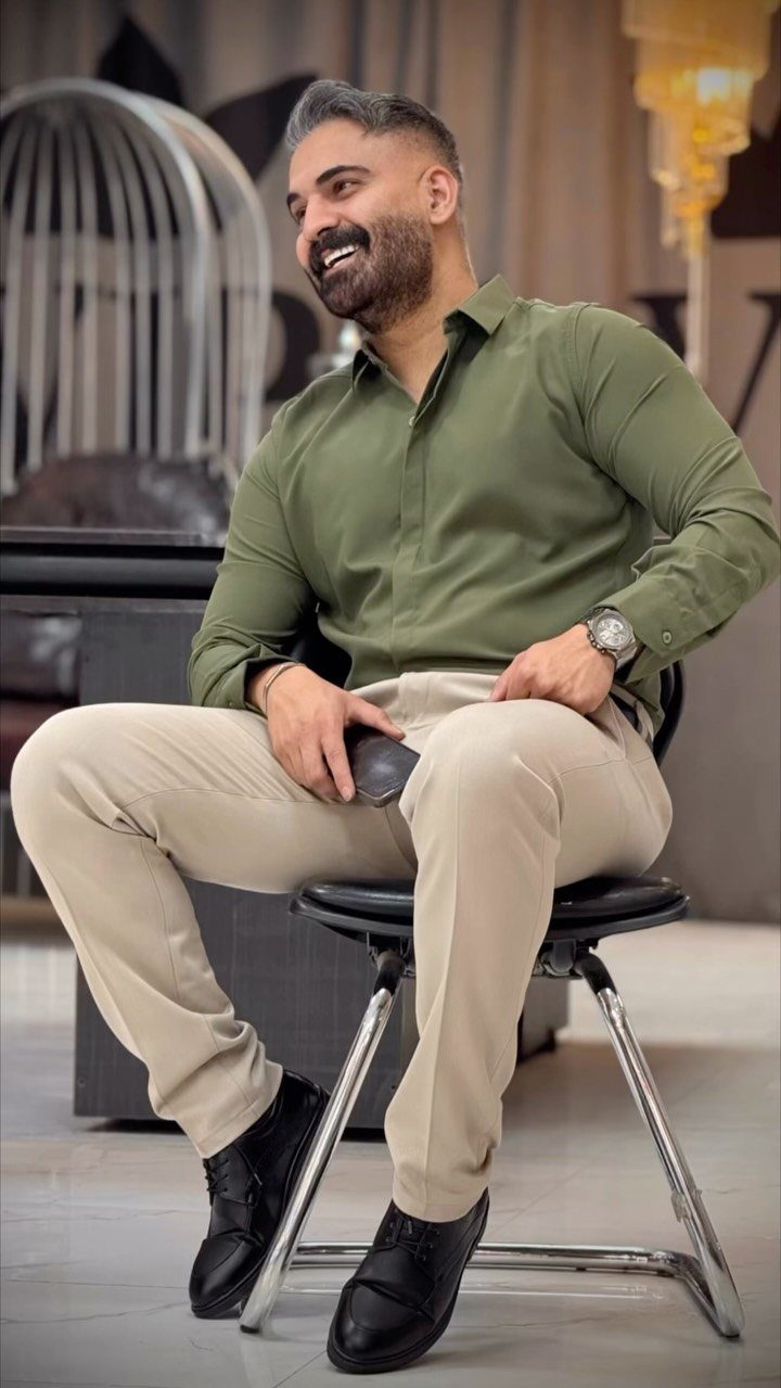 Man in olive green shirt and beige chinos sitting on a chair.