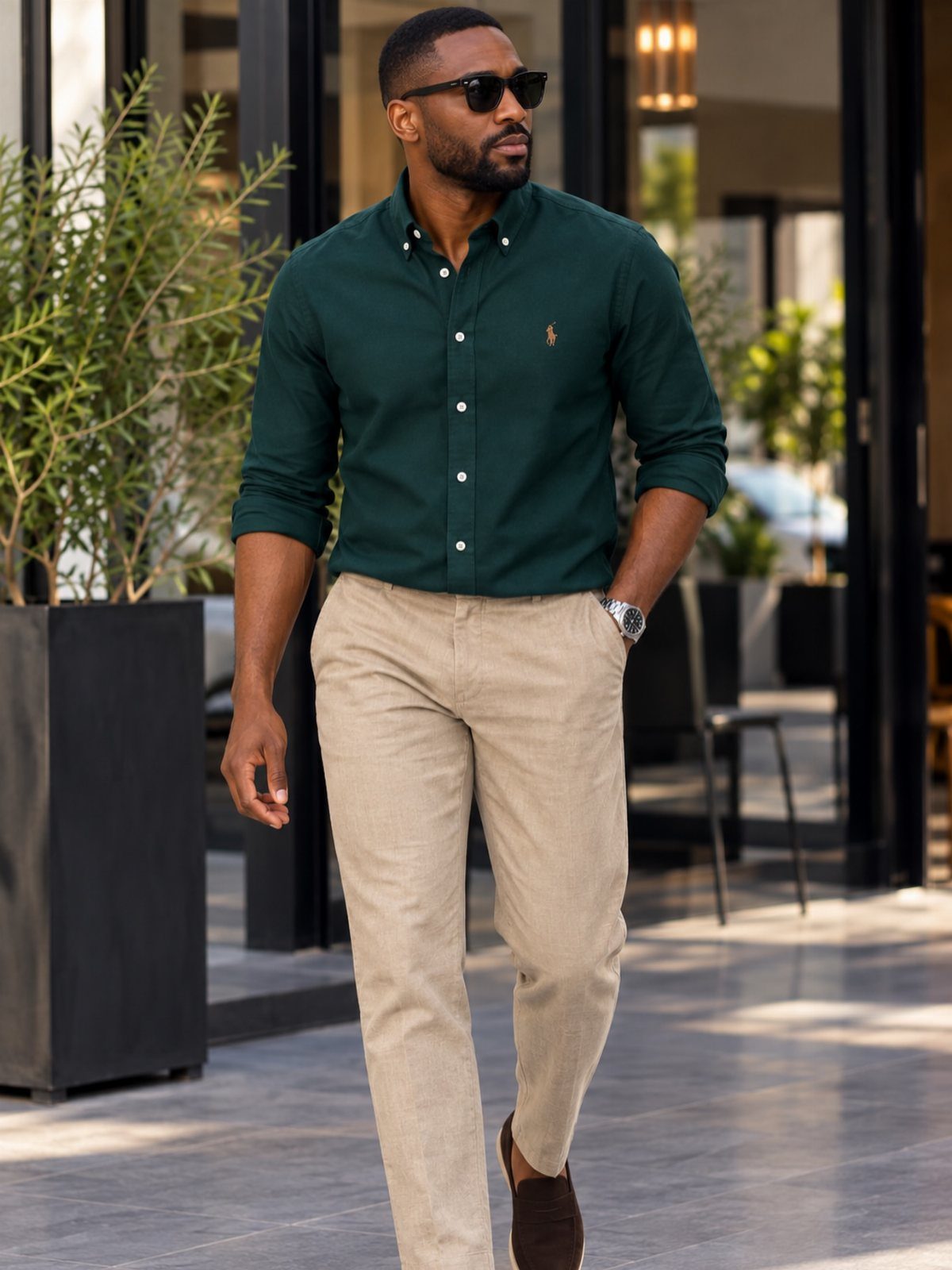Man walking in a dark green button-down shirt, beige chinos, and brown loafers outdoors.