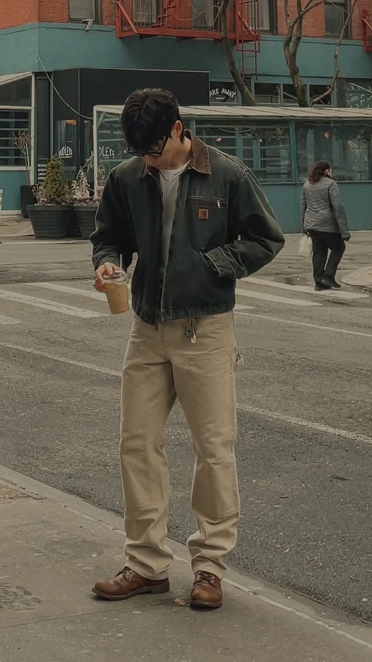 A man in tan carpenter pants and a dark canvas jacket standing on a city street.