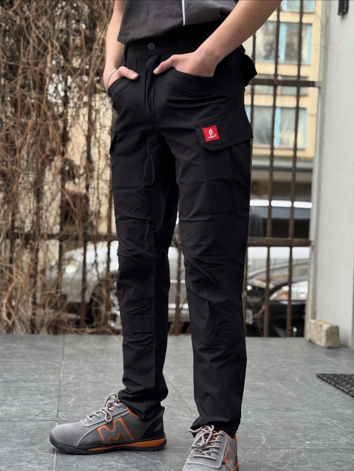 A person wearing black cargo pants and grey work shoes standing on a stone patio.
