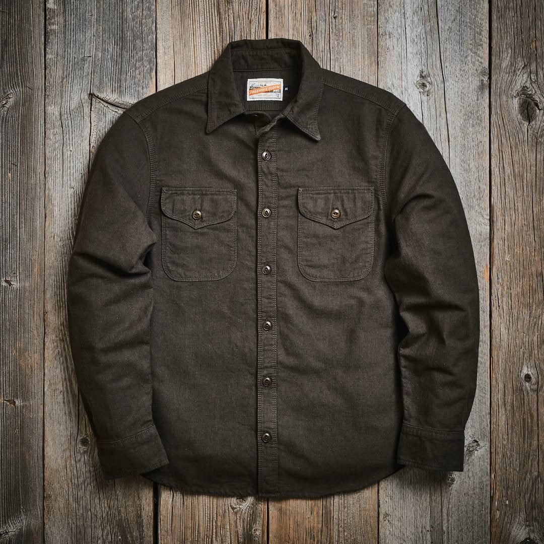 A dark brown button-down work shirt laid flat on a rustic wooden plank surface.