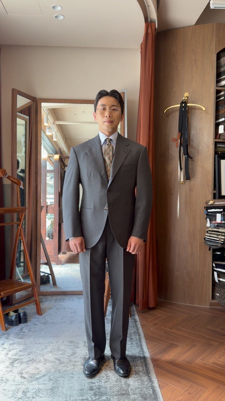 A man posing in a charcoal grey suit with a patterned tie and white shirt.