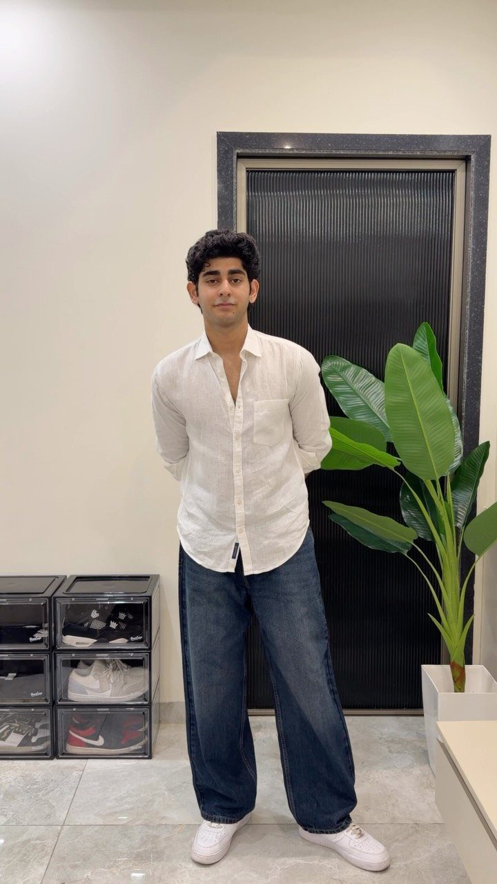 A man wearing a white shirt and wide-leg blue denim jeans standing indoors.