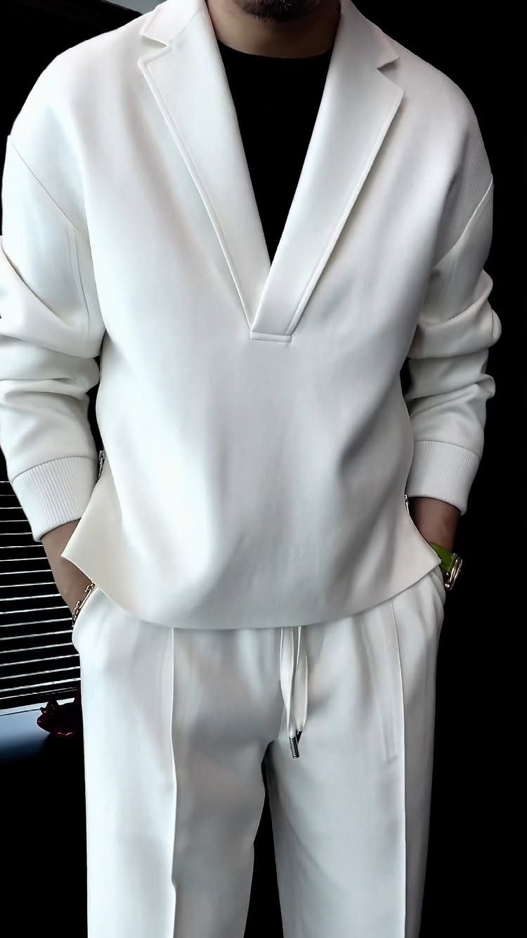Man wearing a structured white V-neck top and matching white trousers in a monochrome outfit.