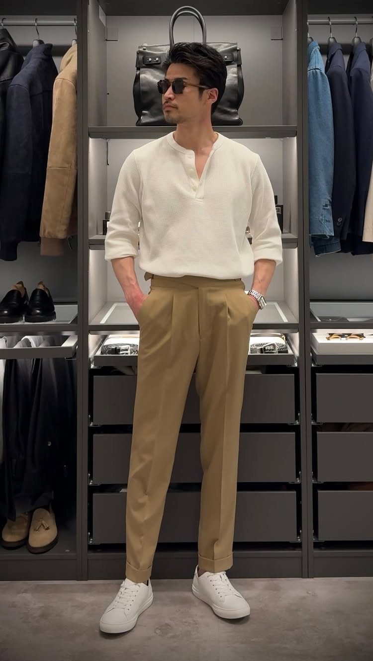 A man in a white henley and tan trousers posing in a modern walk-in closet.